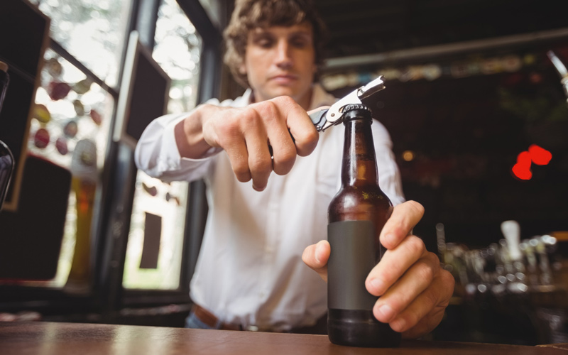 Der Barkeeper öffnet das Bier mit einem Flaschenöffner